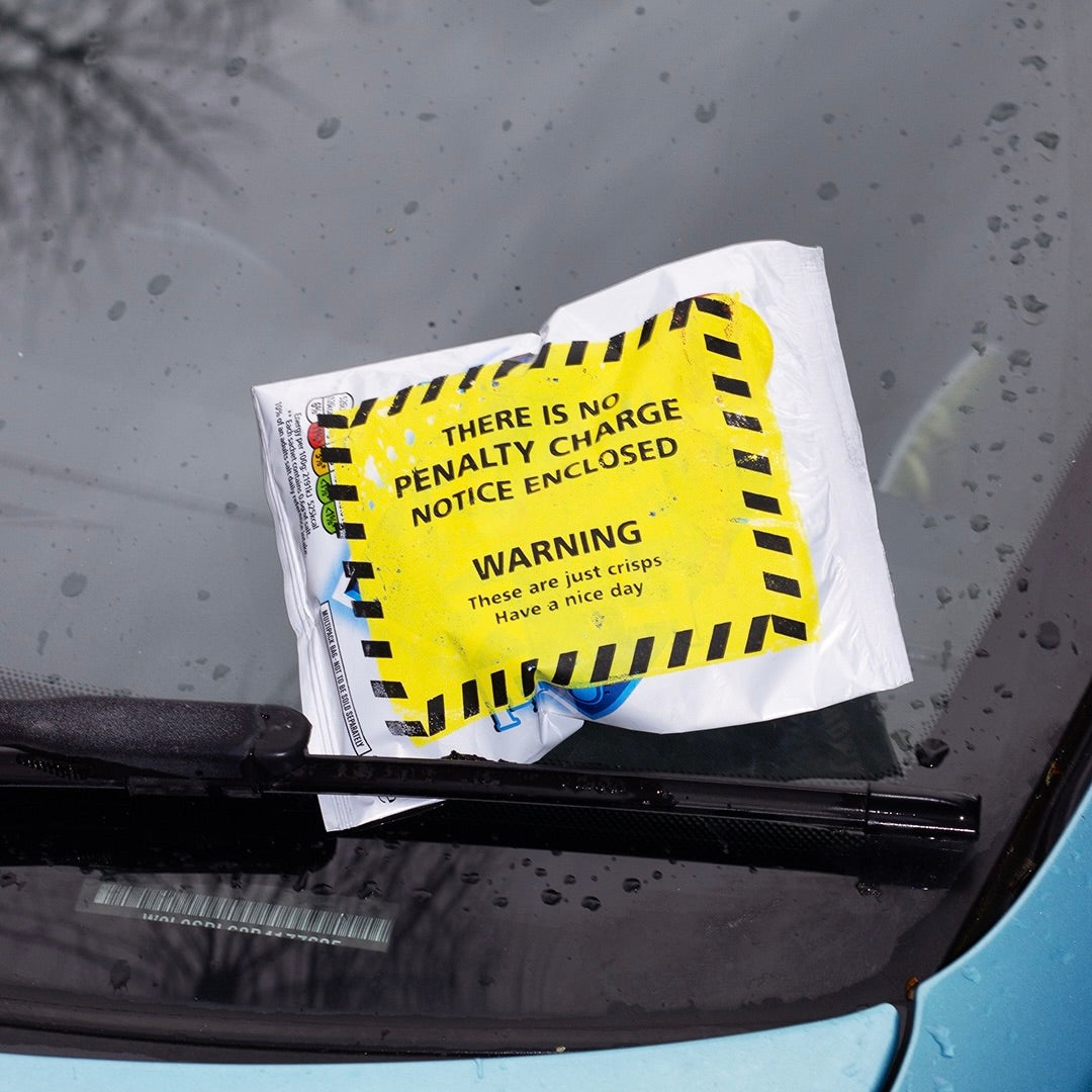 A parody parking ticket placed under a car windshield wiper, styled like an official notice but containing snacks instead of a fine. Part of the SWOPROJECTS “Inspiration Violation” campaign encouraging creatives to take action on unfinished ideas with humor and urgency.