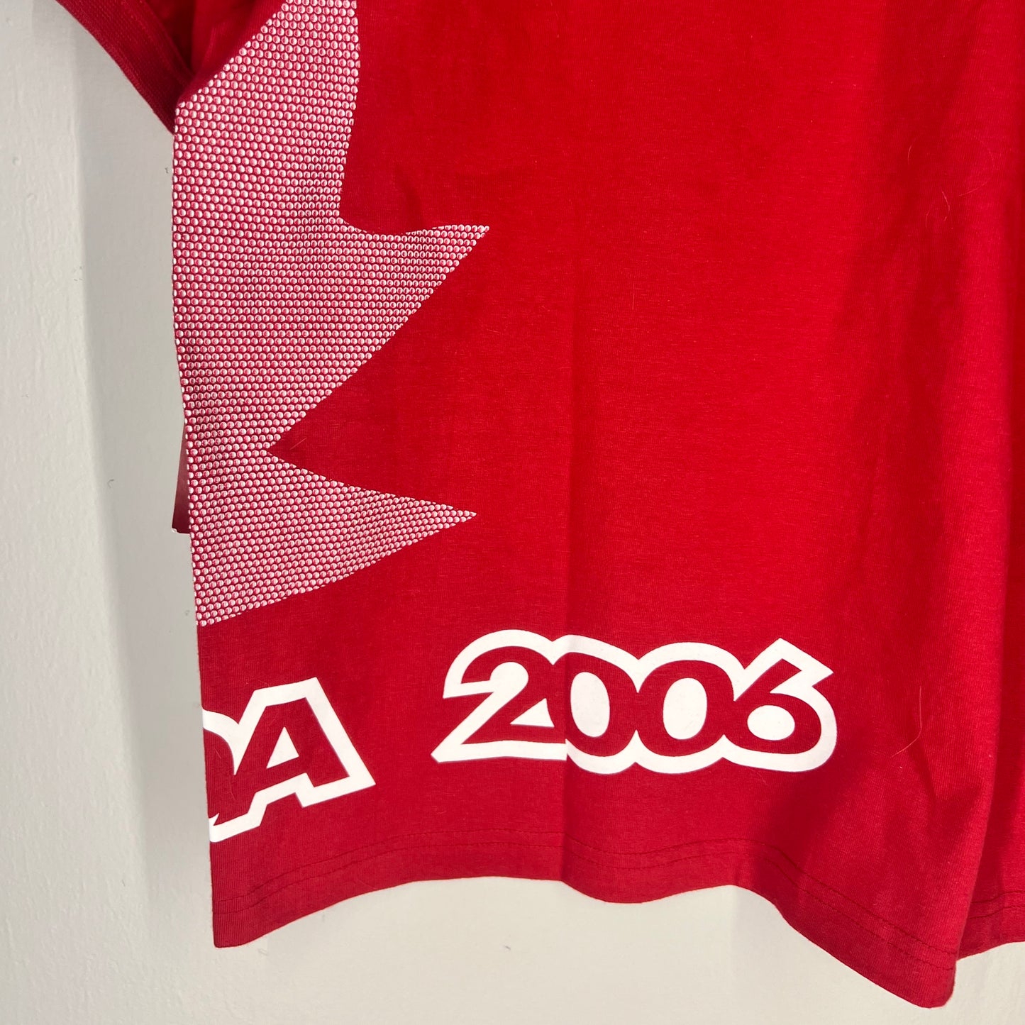 Close-up of lower back hem with 2006 text print and maple leaf graphic.
