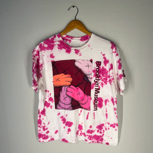 Front view of KAWS What Party x Brooklyn Museum pink/white tie‑dye T‑shirt on hanger