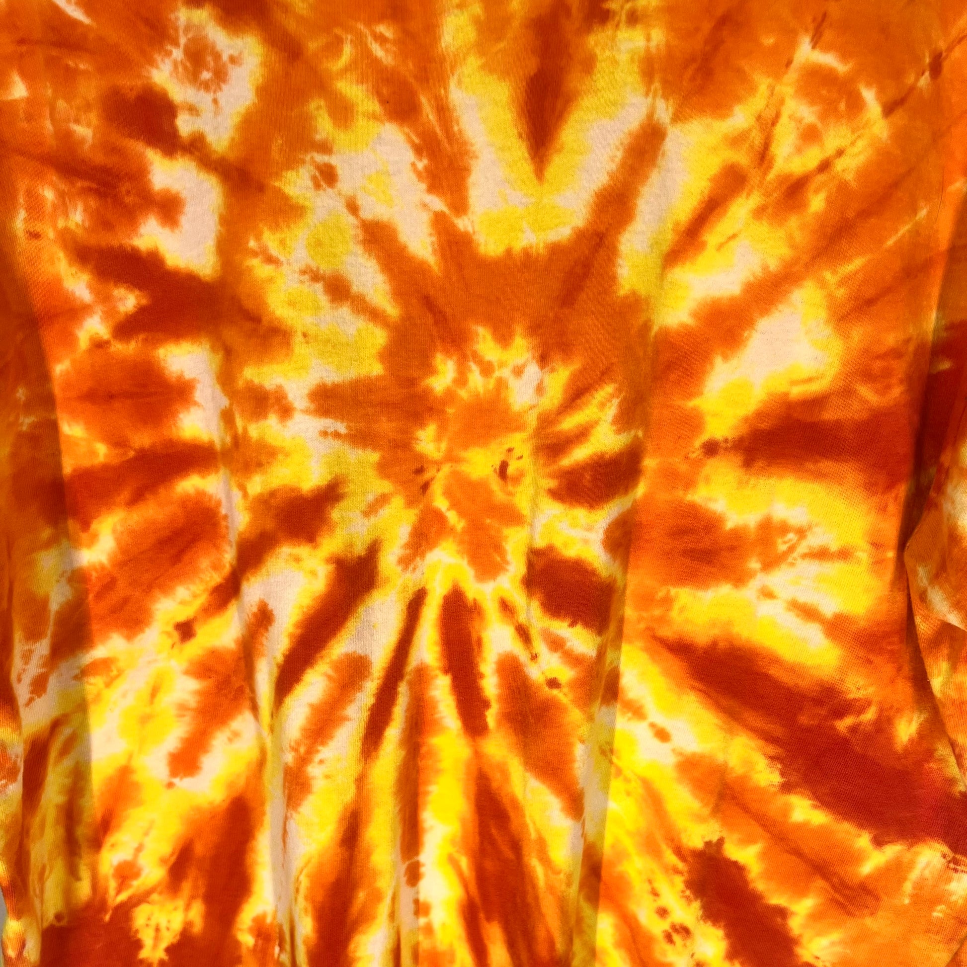 Close-up of orange and yellow tie-dye spiral pattern on shirt fabric